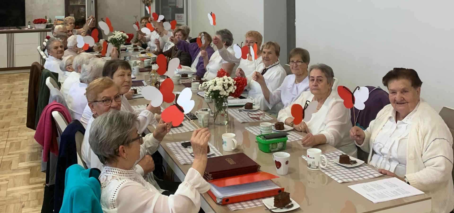 Seniorzy siedzą przy stole z dekoracjami w kolorach narodowych